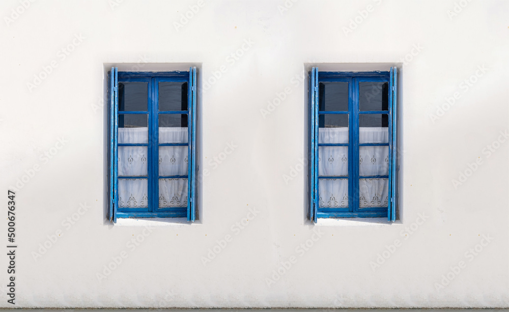 Two windows with open shutters on white wall. Greek island house front view