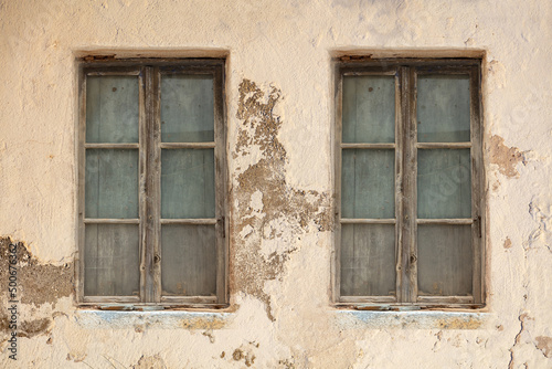 Derelict home. Two window weathered aged on peeled wall. Abandoned shabby worn building exterior