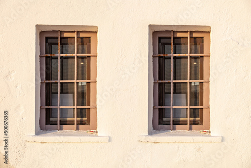 Two old windows and banister metal railing on white wall background. House security, front view