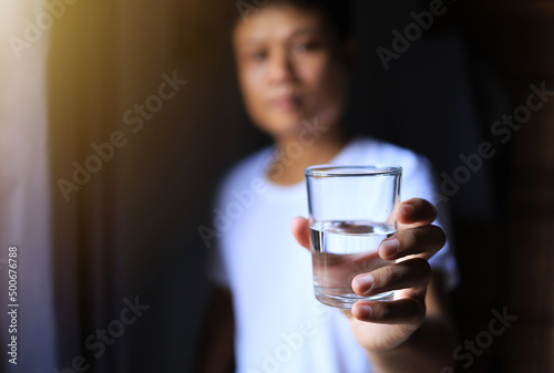 The asian man in a white shirt holding a glass of purify water in the morning after wake up. healthy concept. water drinking in the hot weather.