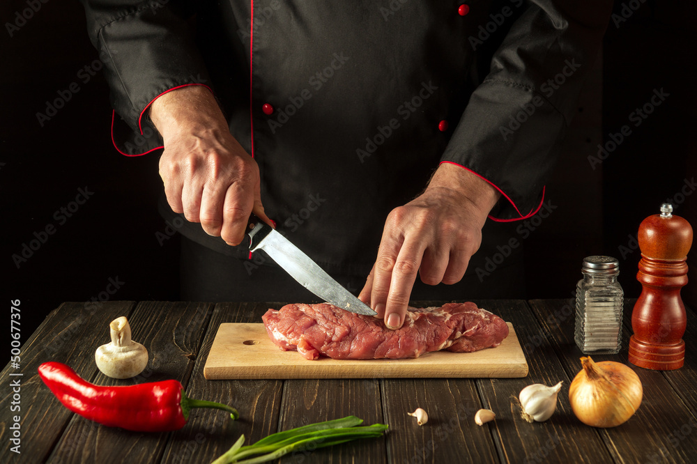 The chef cuts raw beef meat on a cutting board before baking. European cuisine. Hotel menu recipe idea