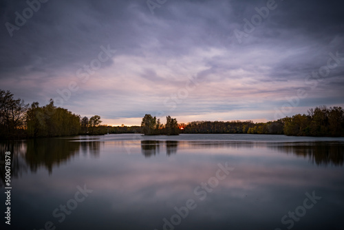 Sunset and clouds in the sky with calm reflection on the water surface at the lake. Natural landscape photo of a lake in Bavaria, Germany.
