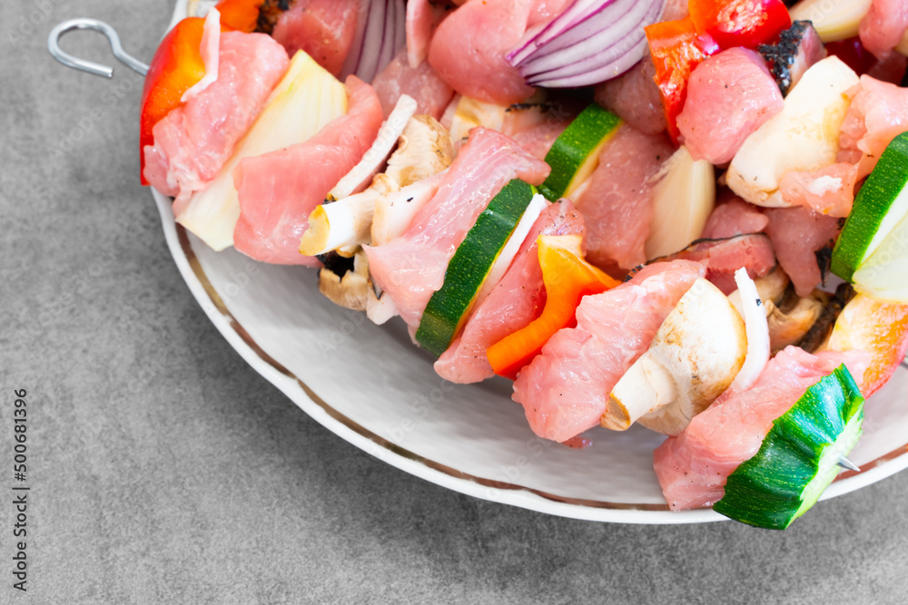 Raw turkey shish kebab on metal skewers, with lots of colorful veggies, on a white plate, ready for preparation. Light grey design desk surface. Delicious, light, great looking food. Raw turkey shish kebab on metal skewers, with lots of colorful veggies, on a white plate, ready for preparation. Light grey design desk surface. Delicious, light, great looking food.