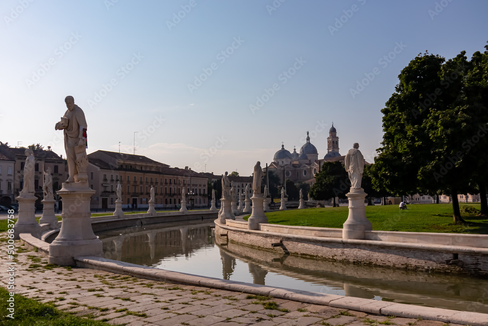 Scenic view on Prato della Valle, square in the city of Padua, Veneto, Italy, Europe. Green island at center, Isola Memmia surrounded by canal bordered by two rings of statues. Basilica of St Giustina Scenic view on Prato della Valle, square in the city of Padua, Veneto, Italy, Europe. Green island at center, Isola Memmia surrounded by canal bordered by two rings of statues. Basilica of St Giustina
