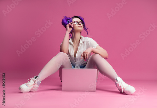 sexy girl with glasses and purple hair with a laptop on a pink background
