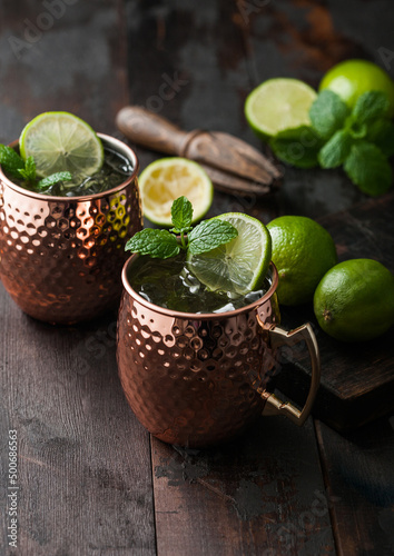 Foto Moscow mule cocktail in a copper mug with lime and mint and wooden squeezer on dark wooden background