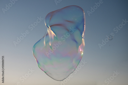 Big bubble flying over blue sky. Huge colorful soap bubbles fly over cloudy sky background.
