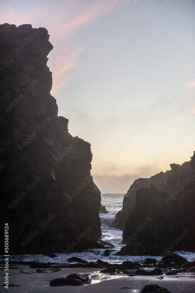 Setting sun behind the rocks at Pfeiffer Beach with orange clouds in the sky.
