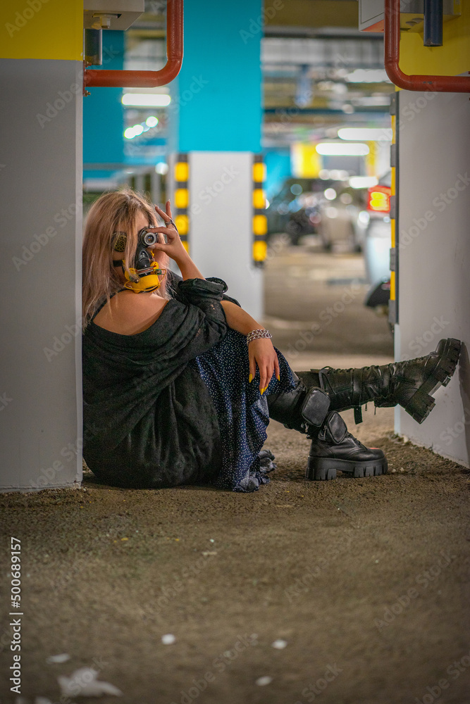 cyborg witch in cyberpunk goggles and a custom respirator, long dress, big natural breasts and deep cleavage in an underground parking lot. Science fiction the distant future post-apocalypse