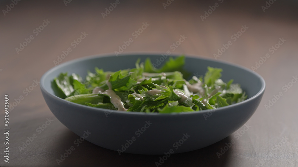 making salad, pour dressing over frisee lettuce in blue bowl on wood table making salad, pour dressing over frisee lettuce in blue bowl on wood table