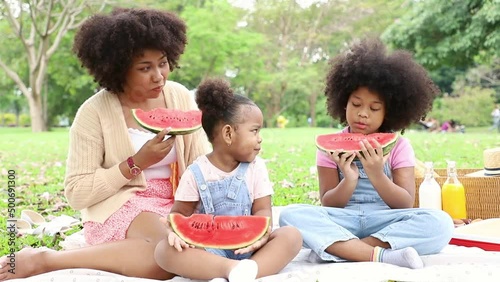 Beautiful mom and her daughter holding pieces of watermelon while picnic at the park. Concept of relaxing and special holiday with family
