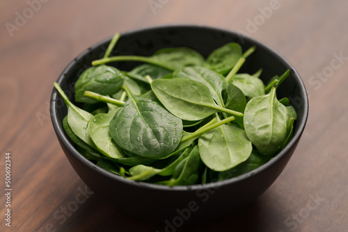 Fresh spinach leaves in black bowl on walnut wood table