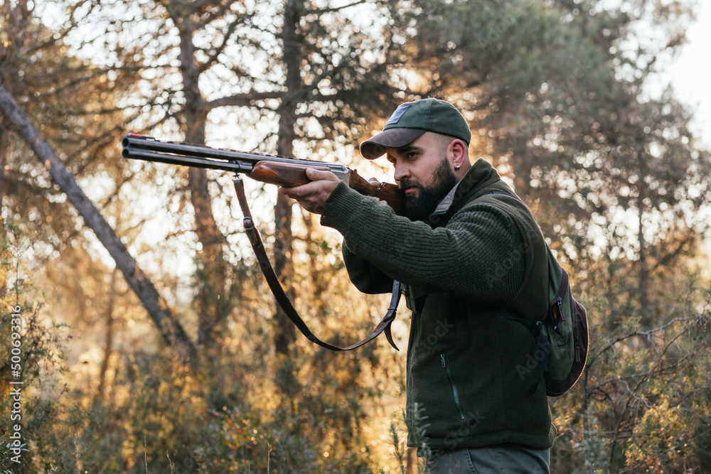 Bearded man aiming rifle while hunting in forest