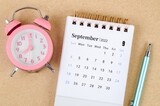 September 2022 Desk calendar with pink alarm clock on brown background.