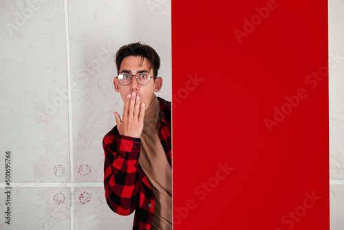 Surprised man in a shirt holds a red billboard with two hands. Promotion student.