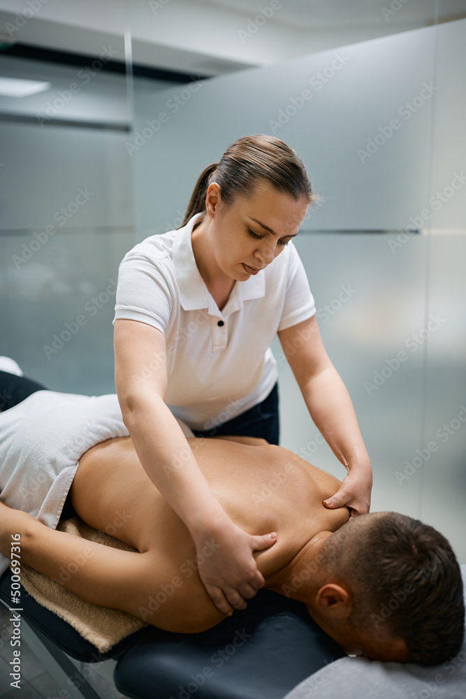 Fototapeta premium Female massage therapist massaging man's shoulder at physical therapy center.