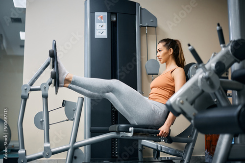 Young female athlete exercises on leg press machine in health club.