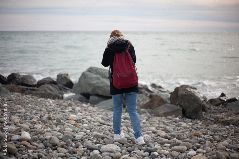 Girl takes pictures of seashore. Woman photographer. Search for story for frame. Big stones. Rocky beach.