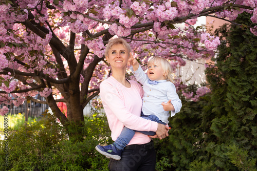 mother and little baby boy son having fun in spring park near pink sakura blooming tree. Spring concept