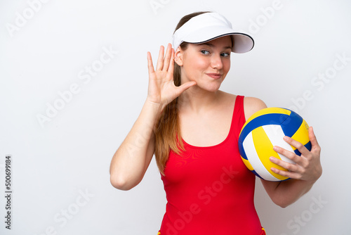 Young caucasian woman playing volleyball isolated on white background listening to something by putting hand on the ear