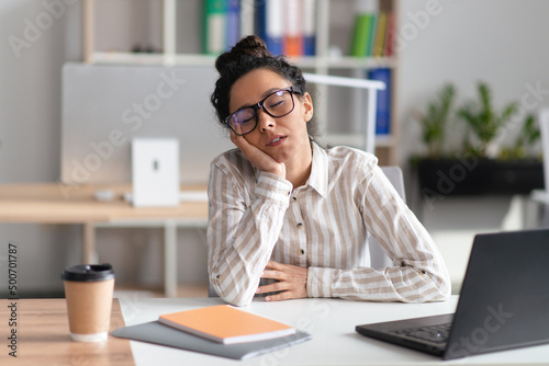 Tired businesswoman sleeping at workplace while working at laptop computer in modern office interior