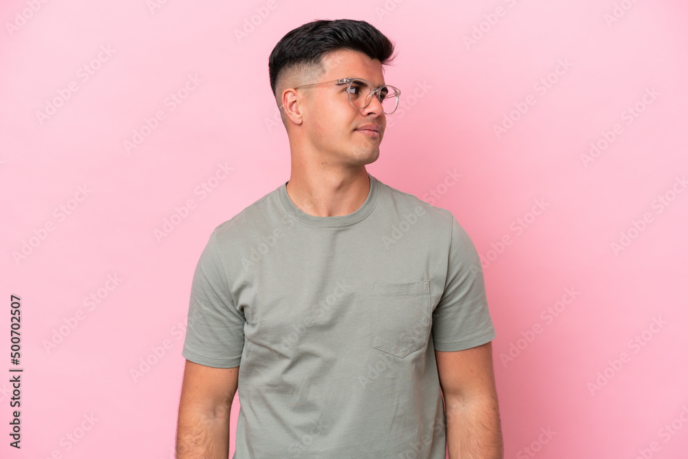 Young caucasian handsome man isolated on pink background making doubts gesture looking side Young caucasian handsome man isolated on pink background making doubts gesture looking side