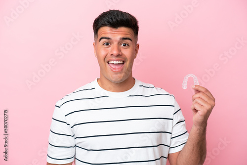 Young caucasian man holding invisaling isolated on pink background with surprise and shocked facial expression photo