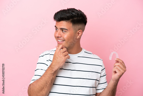 Young caucasian man holding invisaling isolated on pink background thinking an idea and looking side photo