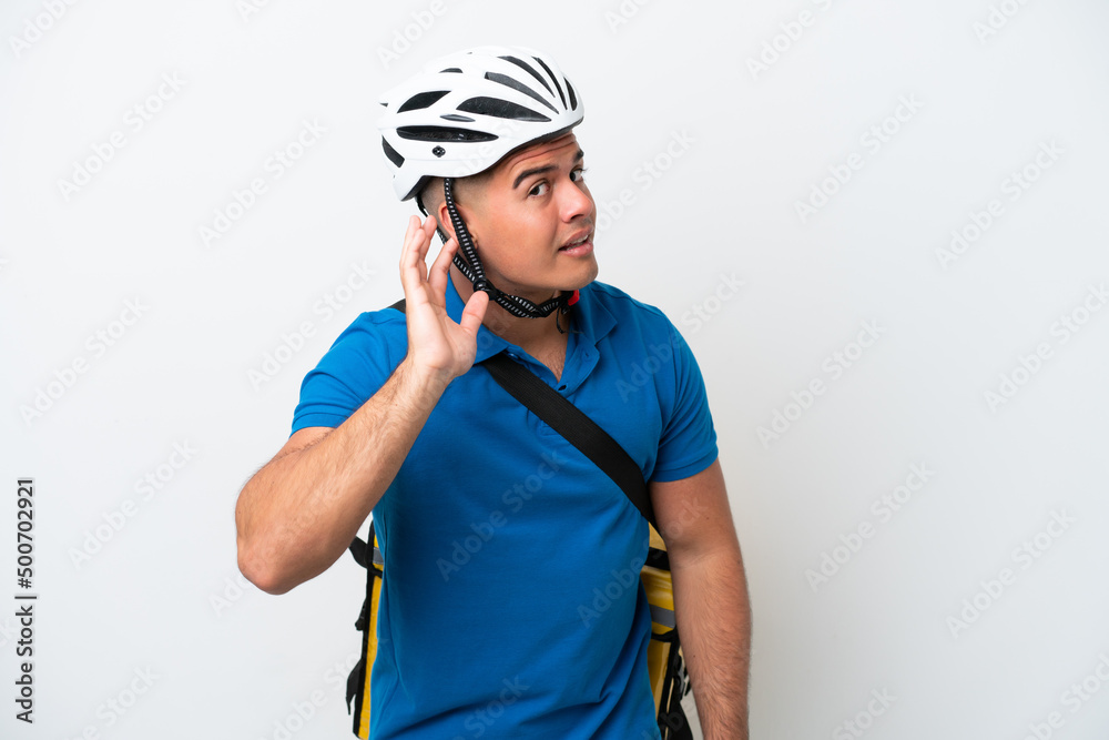 Young caucasian man with thermal backpack isolated on white background listening to something by putting hand on the ear Young caucasian man with thermal backpack isolated on white background listening to something by putting hand on the ear