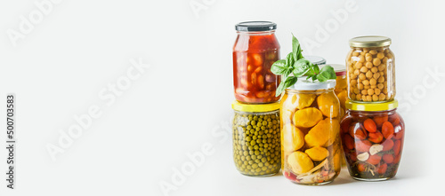 Banner with various preserved pickled tasty vegetables: tomatoes, peas, chickpeas, beans and little pumpkins in glass jars at white background. Front view with copy space.