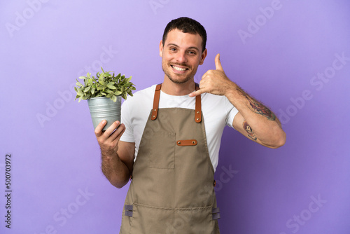Brazilian Gardener man holding a plant over isolated purple background making phone gesture. Call me back sign