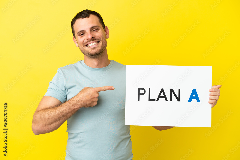 Brazilian man over isolated purple background holding a placard with the message PLAN A and pointing it Brazilian man over isolated purple background holding a placard with the message PLAN A and pointing it
