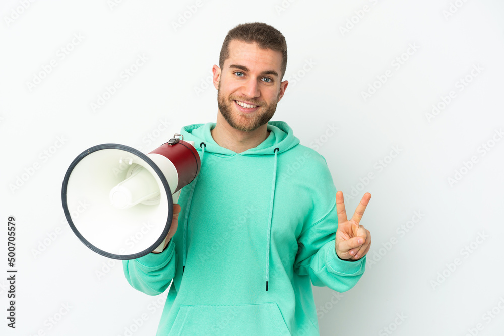 Young handsome caucasian man isolated on white background holding a megaphone and smiling and showing victory sign Young handsome caucasian man isolated on white background holding a megaphone and smiling and showing victory sign