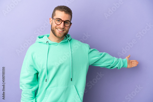 Young handsome caucasian man isolated on purple background extending hands to the side for inviting to come © luismolinero