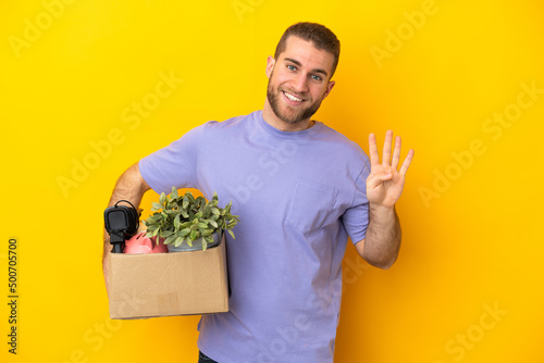 Young caucasian making a move while picking up a box full of things isolated on yellow background happy and counting four with fingers