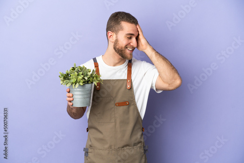 Gardener caucasian man holding a plant isolated on yellow background smiling a lot
