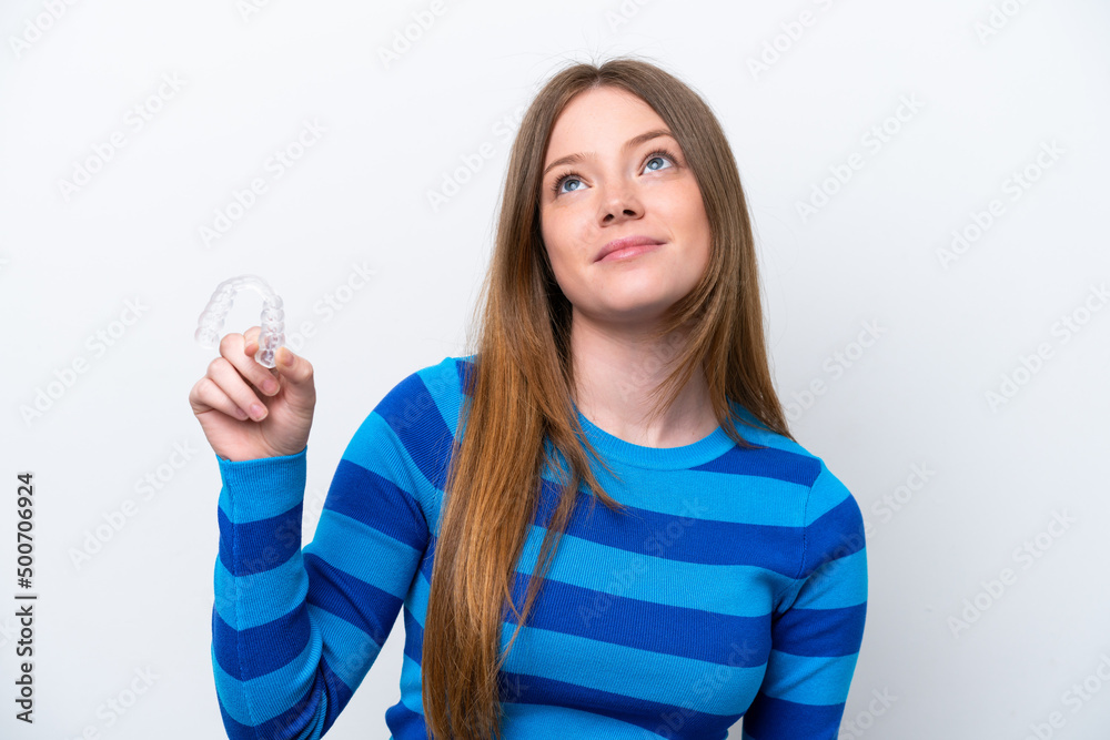 Young caucasian woman holding invisible braces isolated on white background looking up while smiling Young caucasian woman holding invisible braces isolated on white background looking up while smiling