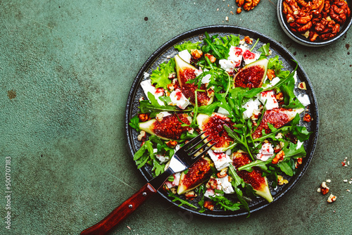 Delicious summer salad with figs, feta cheese, walnuts, arugula and sweet  jam dressing on rusty green table background, top view, negative space