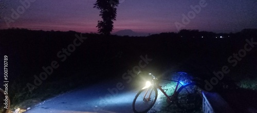 purple morning sky with sillhouete of a hill and a road bike with front lamp photo