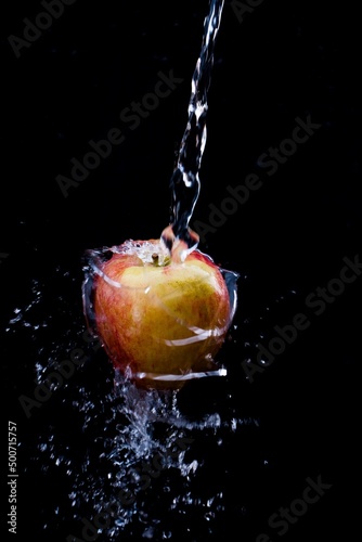 plenty of water is poured over an apple against a black background