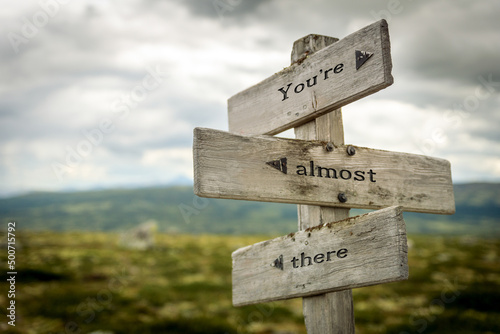 youre almost there text quote written in wooden signpost outdoors in nature. Moody theme feeling. photo