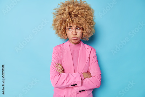 Fotobehang Horizontal shot of upset gloomy woman with curly hair keeps arms folded looks of