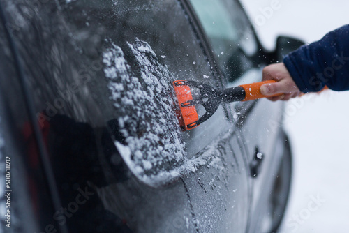 A human hand in a glove cleans a blue car from snow with a special brush. A hand sweeps snow from the hood of the car. Horizontal photo. the consequences of a blizzard