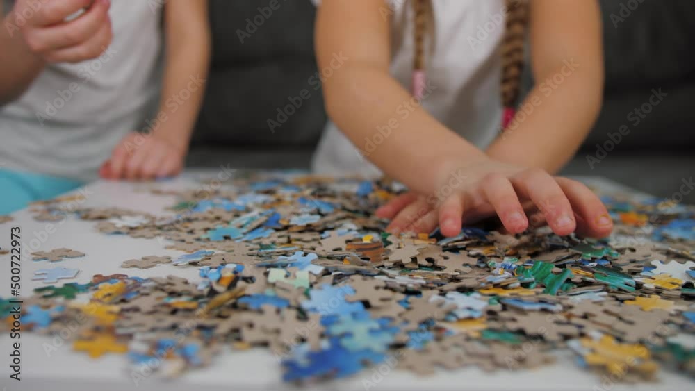 Little girls assemble puzzle details, hands close up. Children collect mosaic together on table or desk, development of fine motor skills and thinking Little girls assemble puzzle details, hands close up. Children collect mosaic together on table or desk, development of fine motor skills and thinking