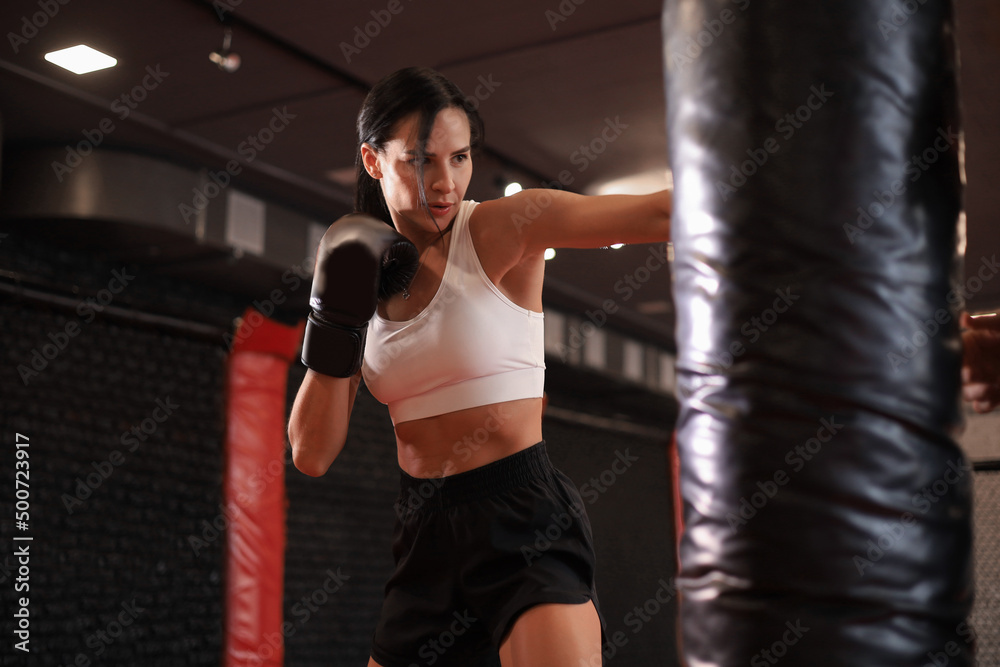 Young woman boxer athletic wearing gloves strikes punching bag during training preparation for battle.