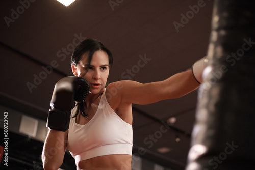 Young woman boxer athletic wearing gloves strikes punching bag during training preparation for battle. © ty