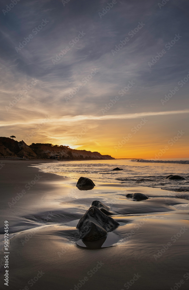 Rocks on the ocean beach with the sunset  sky in the background in Faro, Portugal