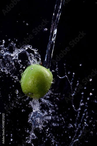 green apple is doused with plenty of water against a black background
