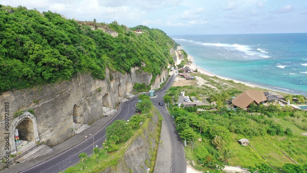Beautiful coastline beach with a white lighthouse, roads and tourist clubs on a sunny day. Aerial landscape of Pandawa Beach, Bali, Indonesia. Bird's-eye view of Ocean landscape.