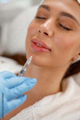 Closeup of young woman getting rejuvenating injections in lips at beauty salon. Cosmetology